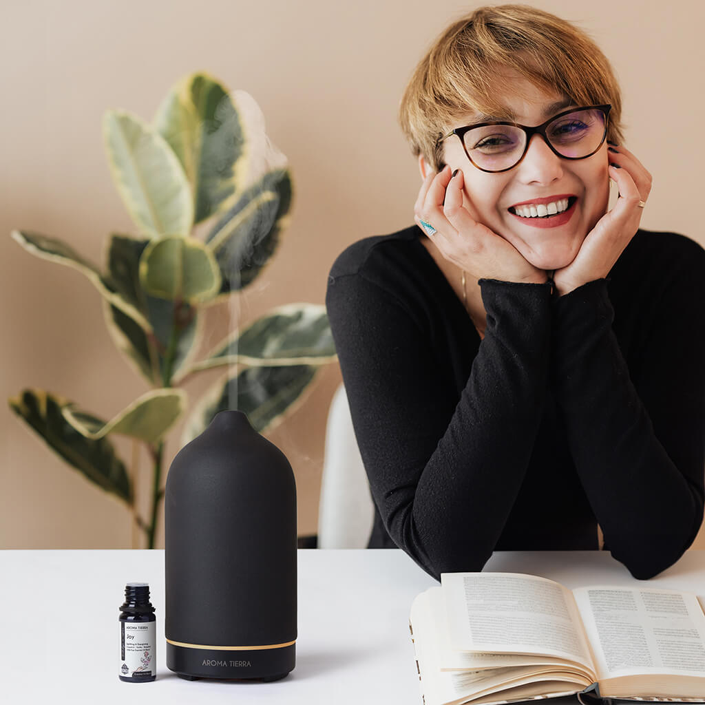 Lady using Joy essential oil blend in diffuser at her desk to boost mood