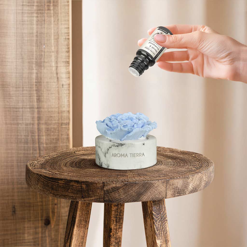 hand adding essential oil to cera flora ceramic diffuser in a sunlit room